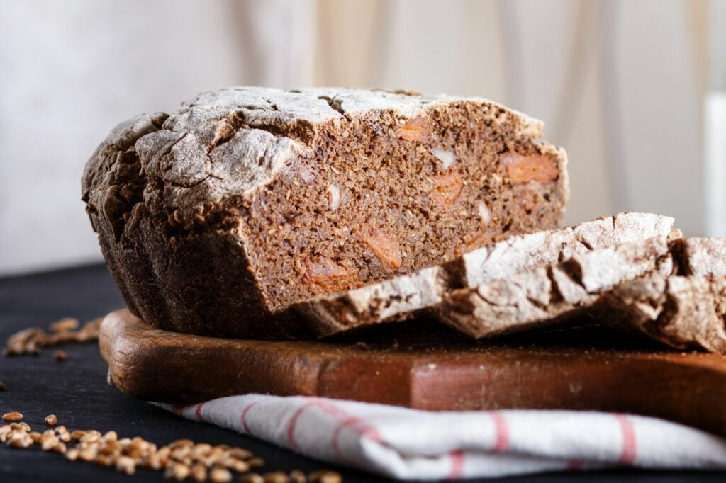 Yeast free homemade sliced bread with whole rye and wheat grains on black wooden background.