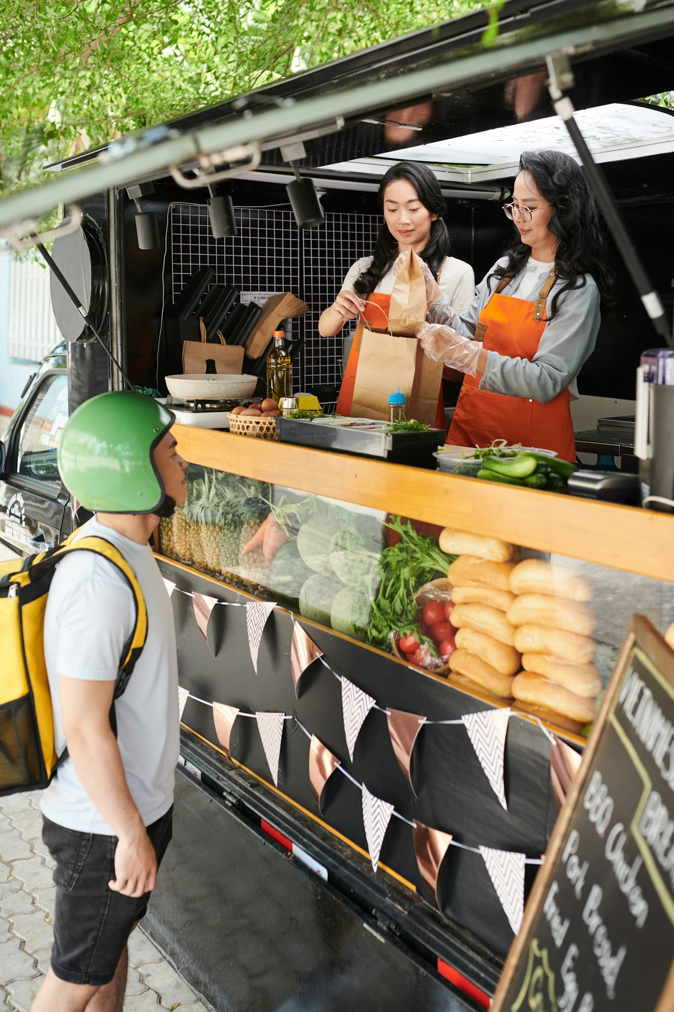 Young deliveryman in protective helmet standing in front of street food van